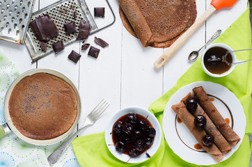 Chocolate pancakes with jam, tea on white wooden background, top view