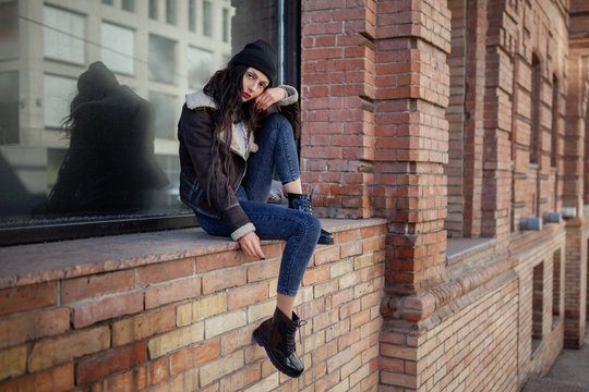 Outdoor lifestyle portrait of pretty young girl, wearing hipster swag grunge style on urban background. Wearing hat and jeans denim. Spring fashion woman. Toned style instagram filters.