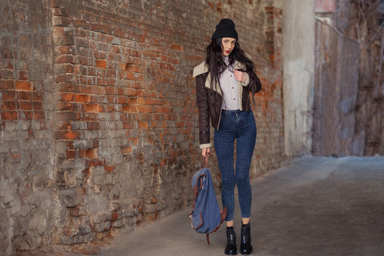 Outdoor lifestyle portrait of pretty young girl, wearing in hipster swag grunge style on urban background. Wearing hat and jeans with backpack. Spring fashion woman. Toned style instagram filters.