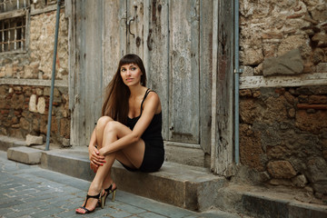 Outdoor lifestyle portrait of pretty young girl, wearing in black dress on urban background. Creative color toned image.