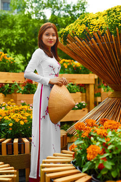 Traditional Clothing Of Vietnam, Asia. Beautiful Happy Asian Girl Dressed In National Traditional Ao Dai Dress ( Costume ), Vietnamese Conical Hat ( Non La, Leaf Hat ) In Flower Garden. Culture.