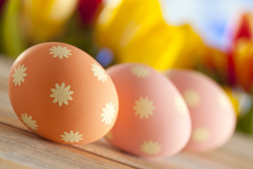 Three Easter eggs on wooden table and colorful tulips in backgro