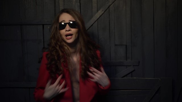 sexy brunette woman in sunglasses and a red jacket on a naked body sings rap
