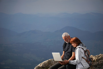Elderly couple using a laptop on top of a mountain