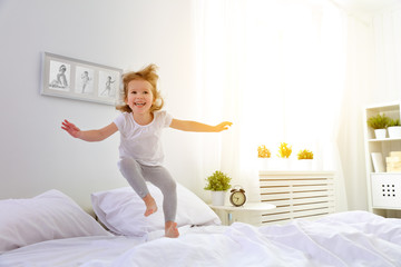 happy child girl jumps and plays bed