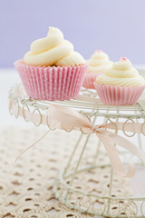 Three vanilla cupcakes with buttercream swirl topping on vintage cake stand