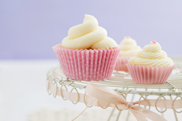 Three vanilla cupcakes with buttercream swirl topping on vintage cake stand