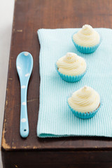 Three vanilla cupcakes with buttercream swirl topping with blue spoon