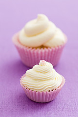 Two vanilla cupcakes with buttercream swirl topping on pink tablecloth
