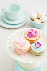 Cupcakes decorated with pink sugar flowers and a sugar butterfly and macarons