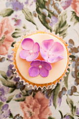 Cupcake decorated with pink sugar flowers on floral background