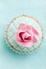 Cupcake decorated with pink sugar flower on turquoise background