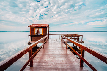 Obraz premium Old wooden pier for fishing, small house shed and beautiful lake