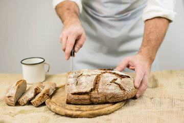 Male cook cuts bread. Rustic style.