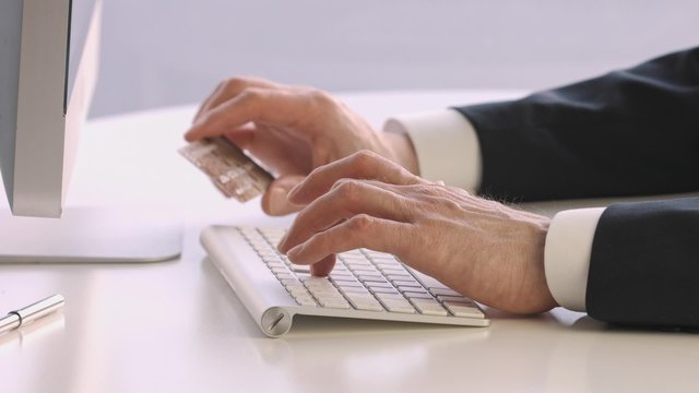 Male hands holding a credit card at a keyboard during online shopping.