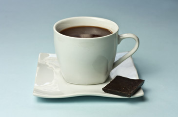 Cup of hot chocolate with piece of chocolate, on blue