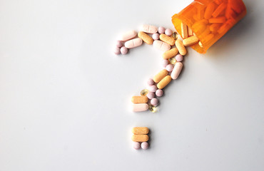 different drugs and health supplement pills in a question mark poured from a medicine bottle - obrazy, fototapety, plakaty