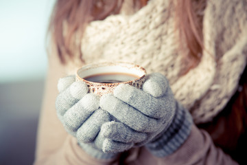 Young woman with mittens holds a coffee cup