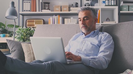 Businessman sitting on the sofa at home, he is smiling and relaxing with hands behind head after working with his laptop - Powered by Adobe