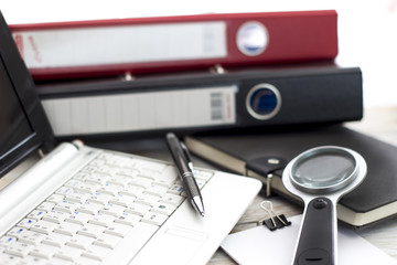 Office workplace with laptop, folders and magnifying glass on wood table