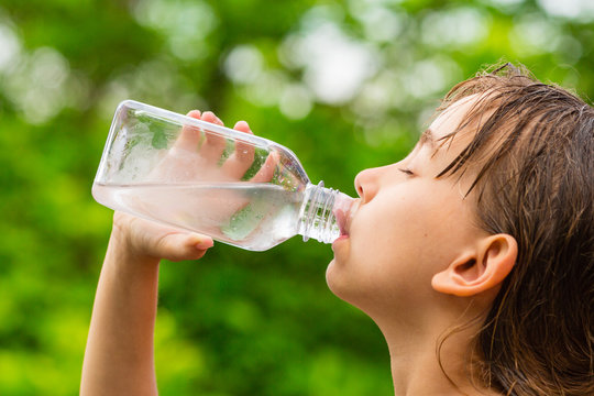Girl drinking clean tap water from transparent glass bottle