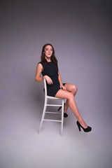 Fototapeta na wymiar Young elegant woman in black dress, shoes. Sitting and posing i
