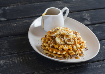 Waffles with banana slices, nuts and caramel sauce on a  wooden background