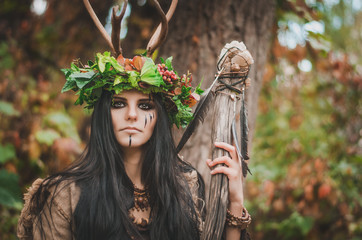 portrait of a beautiful brunette in the form of shaman, with floral wreath on her head and horns