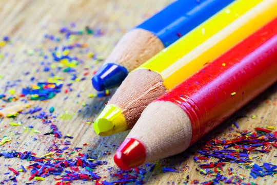 Colorful set of pencils : blue, yellow and red with dust of pencil shavings on a wooden surface.