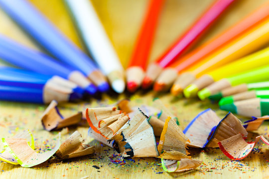Colorful close up set of pencils and pencil shavings on a wooden table.

