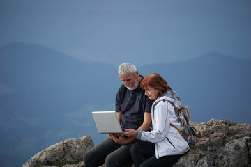 Elderly couple using a laptop on top of a mountain - 104667023