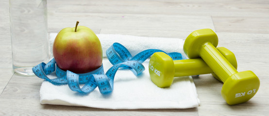 Tasty apple, measure tape and weights on towel