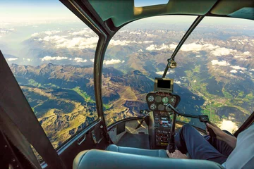 Fotobehang Helikopter Helikoptercockpit die op berglandschap en bewolkte hemel vliegt, met pilootarm die in de cabine rijdt. Spectaculaire luchtfoto van de Alpen bergketen.
