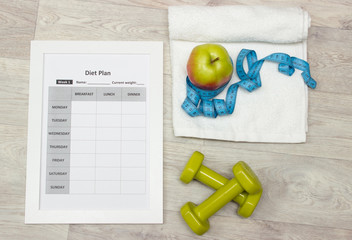 Diet plan, green weights, apple, measure tape and towel