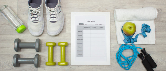 Various sport equipment with diet plan on wooden background
