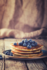 Pancake folded stack of with liquid honey and fresh blueberries on wooden background.Toned image.Vintage style.selective focus.
