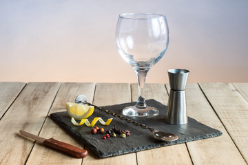 Balloon glass, bar spoon and botanicals for prepare a gin tonic on a wood table.