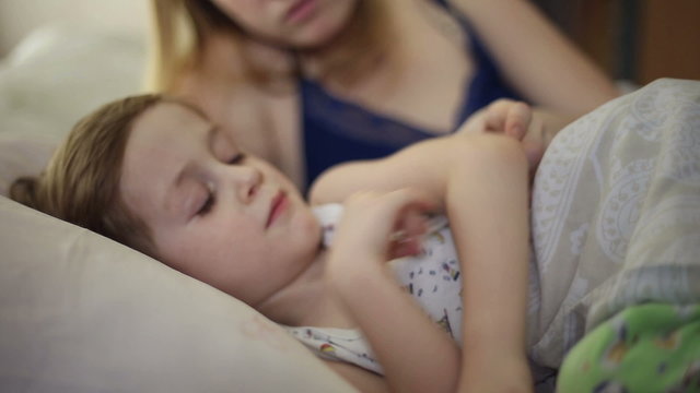 The boy is sick and he has fever and his mom measures his temperature using a thermometer
