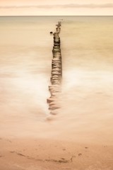 Wooden breakwater on wavy Baltic Sea.  Pink horizon with first hot sun rays.