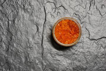 Red caviar in a jar on a stone slab. View from above.
