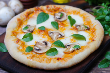 Italian food. Mediterranean cuisine. Delicious pizza with mushrooms and basil - thin pastry crust on wooden background.
