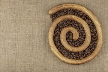 Roasted coffee beans in a wooden spiral on the canvas background. Fresh roasted coffee. Preparing for brewing coffee.
