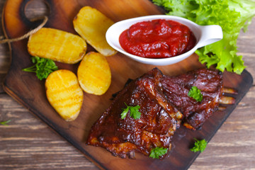 Appetizing rosy and barbecued lamb ribs seasoned with a barbecue sauce and served with fresh herbs and potatoes on an old rustic wooden chopping board