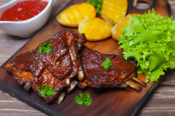 Appetizing rosy and barbecued lamb ribs seasoned with a barbecue sauce and served with fresh herbs and potatoes on an old rustic wooden chopping board
