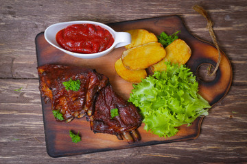 Appetizing rosy and barbecued lamb ribs seasoned with a barbecue sauce and served with fresh herbs and potatoes on an old rustic wooden chopping board