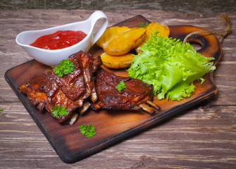 Appetizing rosy and barbecued lamb ribs seasoned with a barbecue sauce and served with fresh herbs and potatoes on an old rustic wooden chopping board
