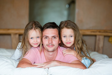 Father with two adorable little girls having fun in bed smiling