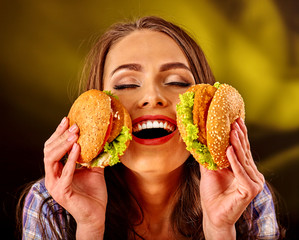 Happy girl keeps big woman small hamburgers. Fastfood concept on green.