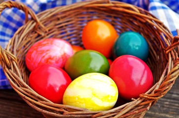 dyed easter eggs in wood basket on rustic wooden background