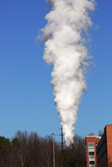 Fototapeta na wymiar white smoke rising up against blue sky from industrial area